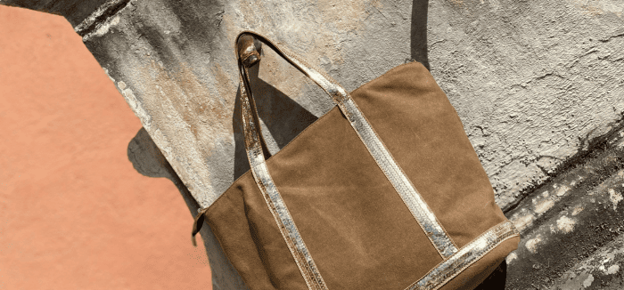 Sac cabas taupe avec bandes scintillantes, posé sur un mur en pierre en extérieur